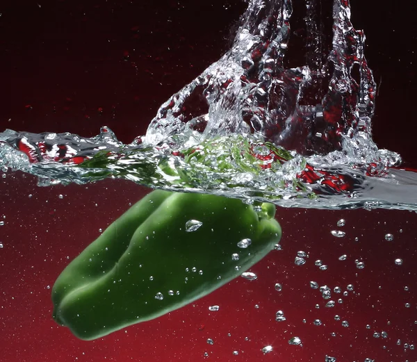Grön paprika faller i vattnet. röd bakgrund — Stockfoto