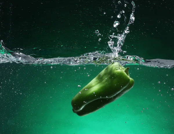 Πράσινο πιπέρι που εμπίπτουν στο νερό. πράσινο φόντο — Φωτογραφία Αρχείου