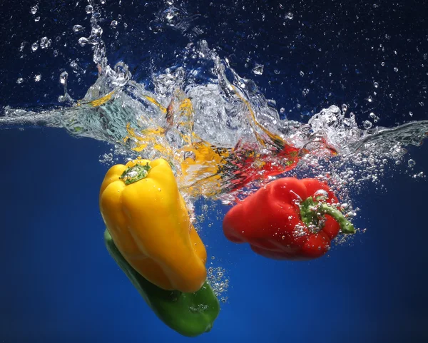 Tři papriky pádu do vody. modré pozadí — Stock fotografie
