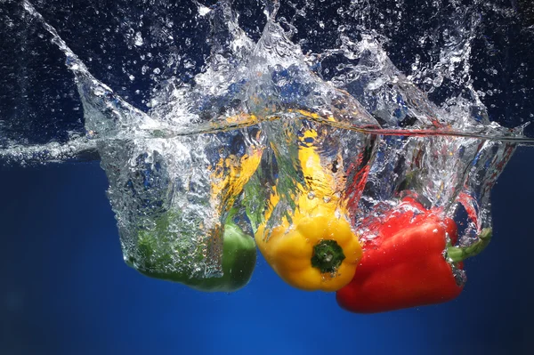 Tre peperoni che cadono in acqua. Fondo blu — Foto Stock