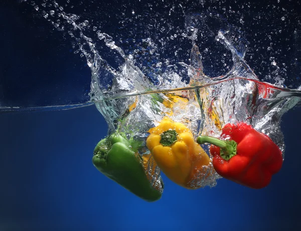 Drei Paprika, die ins Wasser fallen. blauer Hintergrund — Stockfoto