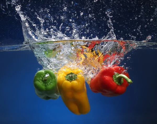 Drei Paprika, die ins Wasser fallen. blauer Hintergrund — Stockfoto