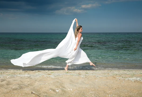 Mujer rubia delgada corre en la playa, con chal blanco —  Fotos de Stock