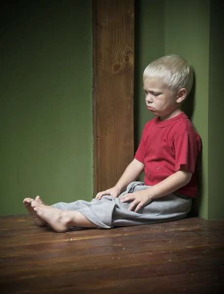 Pequeno menino triste sentar no canto — Fotografia de Stock