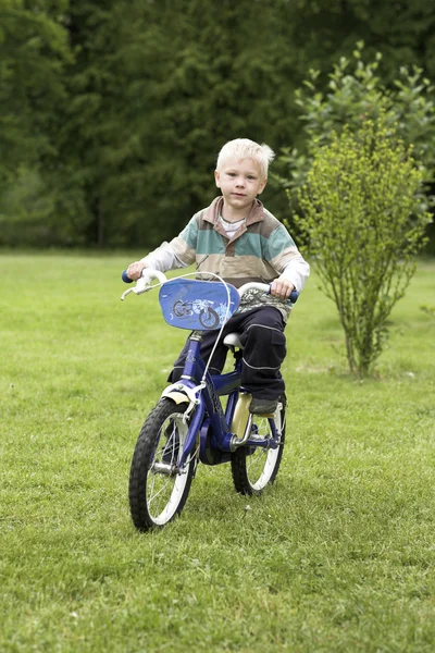 Menino montando uma bicicleta no campo de grama — Fotografia de Stock