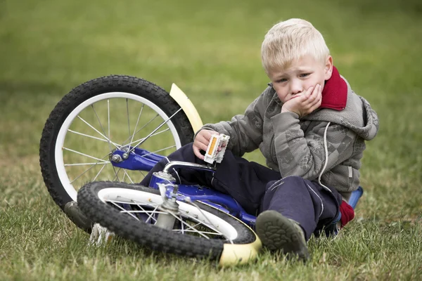 Upprörd liten pojke sitter nära sin cykel — Stockfoto