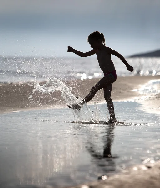 Young girl kicks the water at the beach holiday — Stock Photo, Image