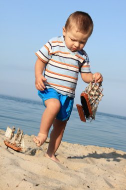Kumsalda küçük bir çocuk ve bir gemi.
