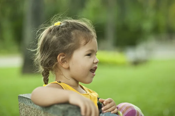Het kleine meisje zit op een bankje op vakantie — Stockfoto