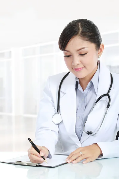 Vrouwelijke arts schrijft op een klembord — Stockfoto