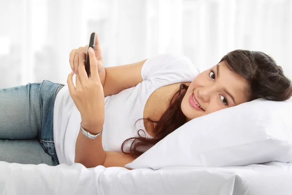 ベッドに横になっている携帯電話で女性のテキスト メッセージ — ストック写真
