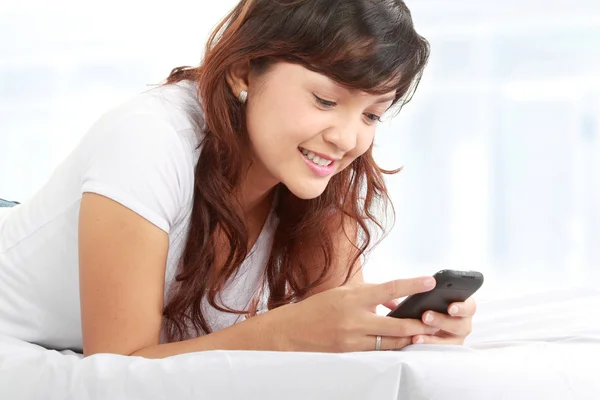 Žena SMS na telefonu ležící na posteli — Stock fotografie