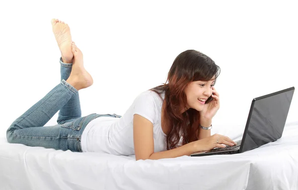 Chica en el teléfono en la cama con el ordenador portátil —  Fotos de Stock