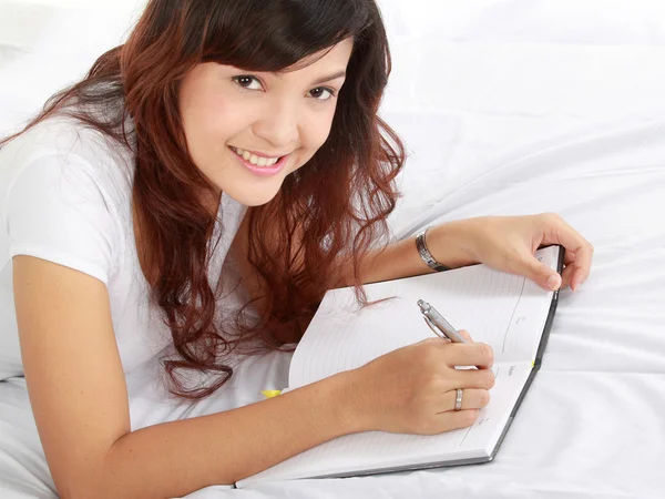 Mädchen schreibt Buch auf dem Bett — Stockfoto
