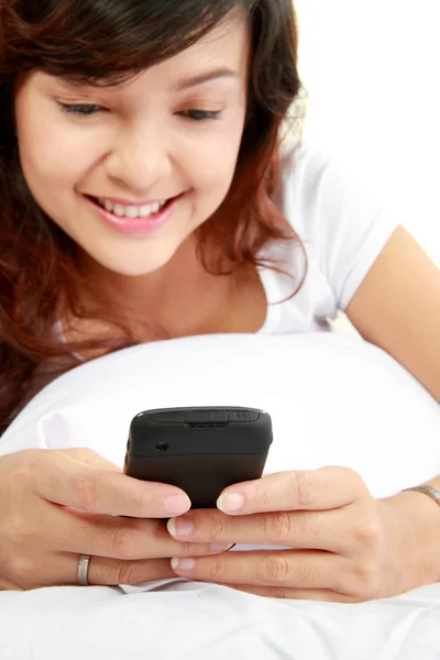 Женщина пишет смс по телефону лежа на кровати — стоковое фото