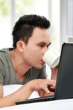 bir yatakta yatarken ve dizüstü bilgisayar kullanan adam