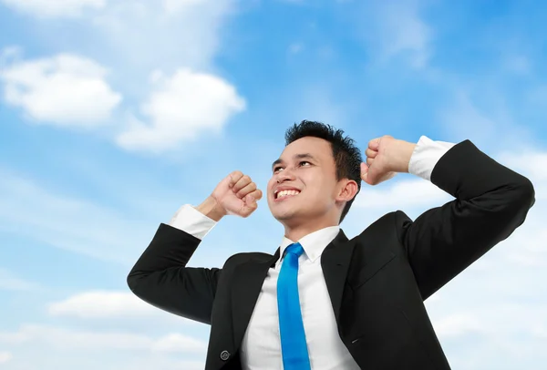 Homem de negócios com braços erguidos sob o céu azul — Fotografia de Stock