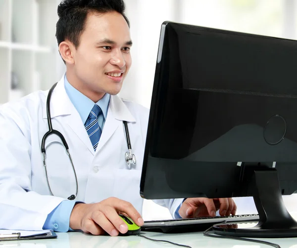 Läkare vid sitt skrivbord framför dator — Stockfoto