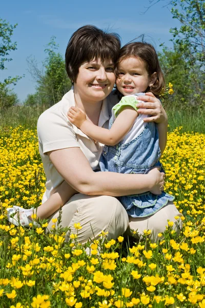 Anne ve kızı sarı çiçekler arasında oturan — Stok fotoğraf