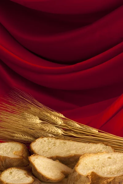 Fette di pane con grano su raso rosso — Foto Stock