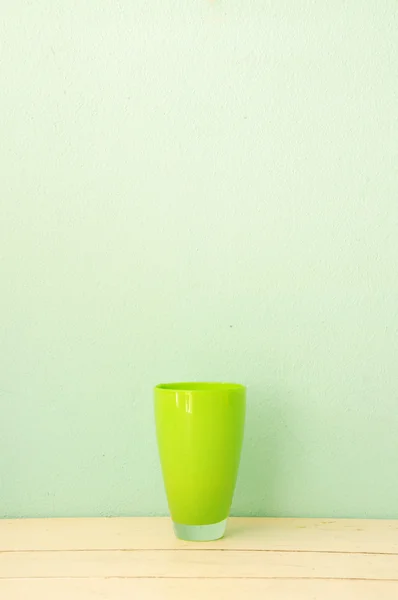 stock image Green glass cup on white wood with green grunge wall