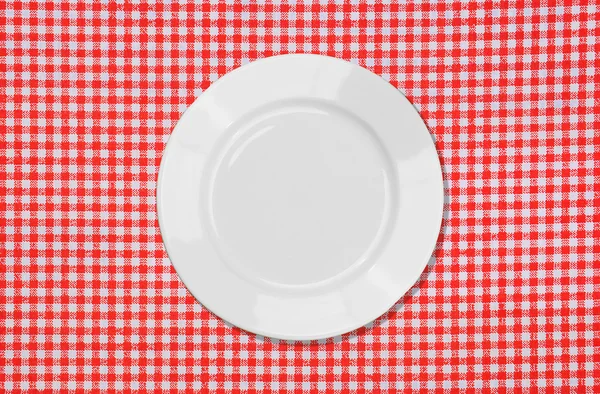 Біла тарілка на червоно-білій скатертині — стокове фото