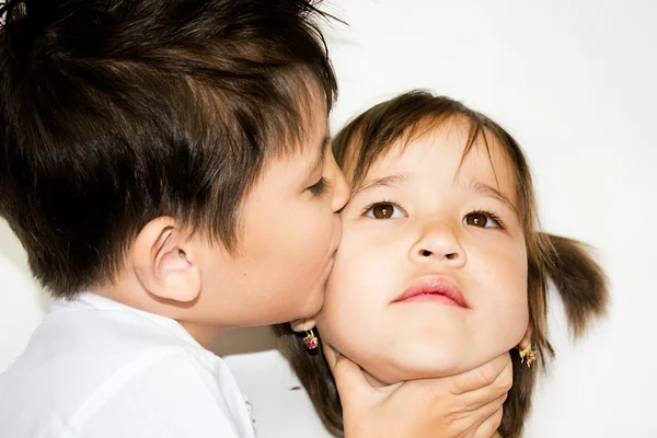 Мальчик целует девушку на белом фоне — стоковое фото