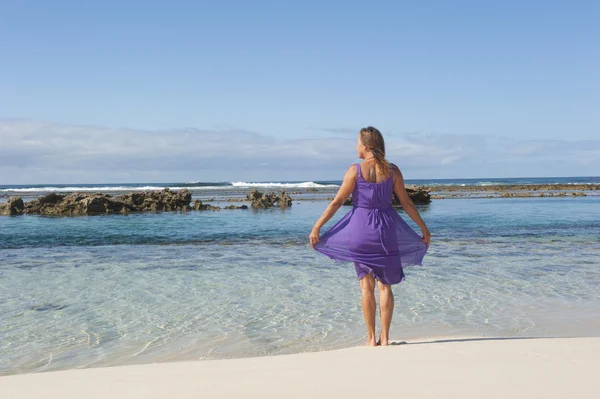 Sexig kvinna i lila klänning glad på stranden — Stockfoto