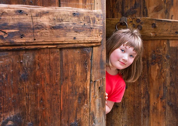 Sevimli kız eski bir ahşap kapı gözetleme — Stok fotoğraf