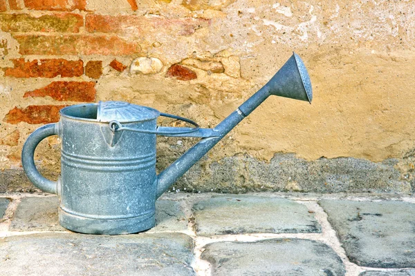 Old metal watering can by a rustic brickwall — Stock Photo, Image