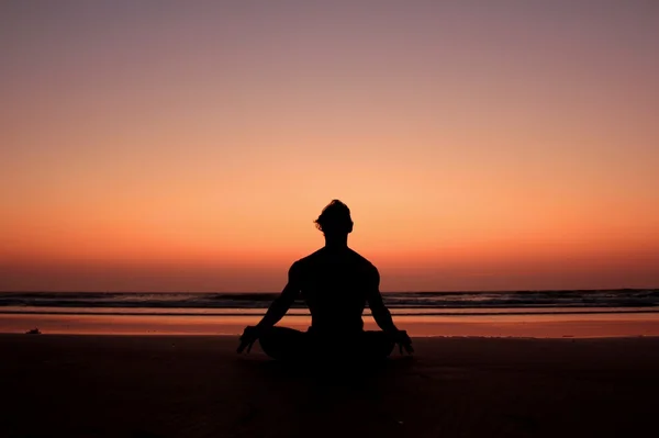 Het silhouet van een man in een yoga pose op de achtergrond van een zonsondergang kust. Meditatie Rechtenvrije Stockfoto's
