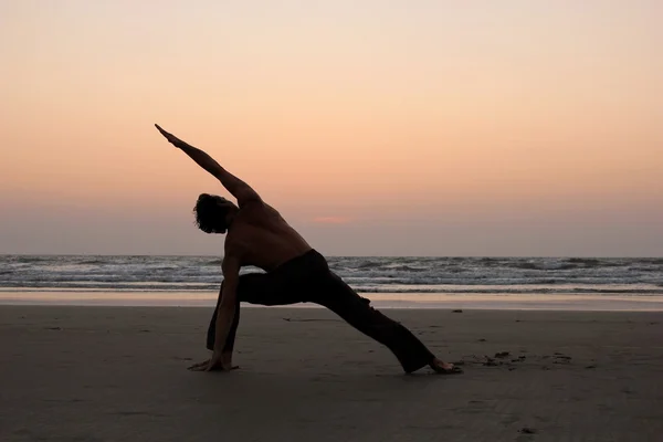 Het silhouet van een man in een yoga pose op de achtergrond van een zonsondergang kust Stockfoto