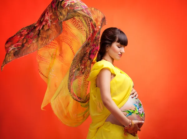 The pregnant girl with the drawn picture on a stomach in a yello — Stock Photo, Image