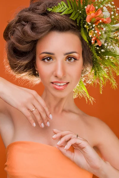 Une belle fille avec des fleurs sur la tête sur un fond orange — Photo