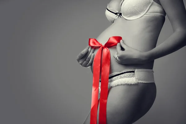 Svartvita foton av gravid mage med en röd rosett i hans h — Stockfoto