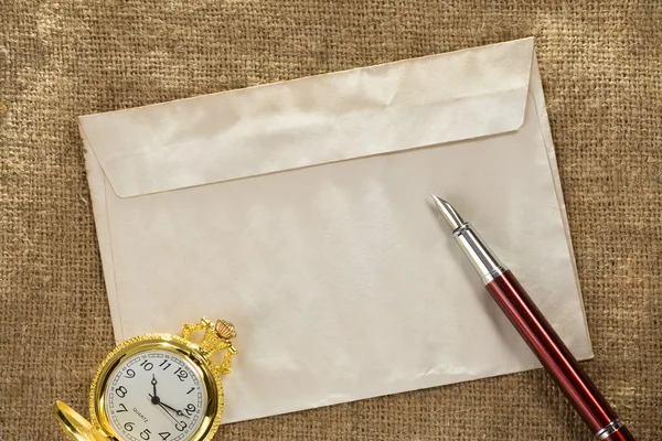 Reloj y pluma de tinta en el sobre en el fondo del saco vintage — Foto de Stock