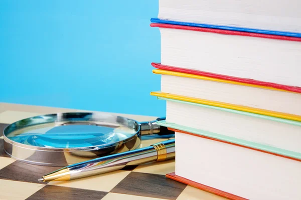 Βιβλία, μεγεθυντικός φακός και στυλό πάνω σε σκακιέρα — Φωτογραφία Αρχείου