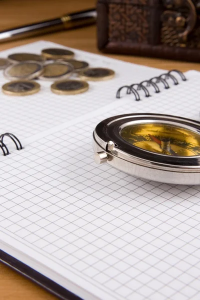 Kompas, pióro i monety na notebooka — Zdjęcie stockowe