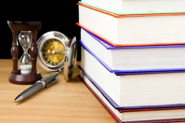 Högen av böcker, penna och timglas på svart — Stockfoto