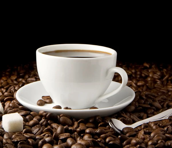 コーヒーのカップ、スプーンと黒に分離された豆 — ストック写真