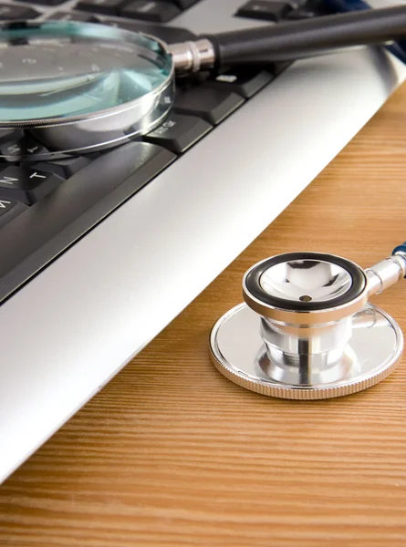 Stethoscope and laptop with magnifier on wood — Stock Photo, Image