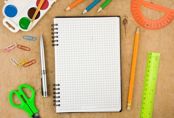 Accesorios escolares y cuaderno comprobado sobre madera — Foto de Stock