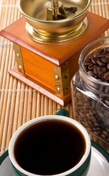 Cup of coffee, pot full of beans and grinder on straw — Stock Photo, Image