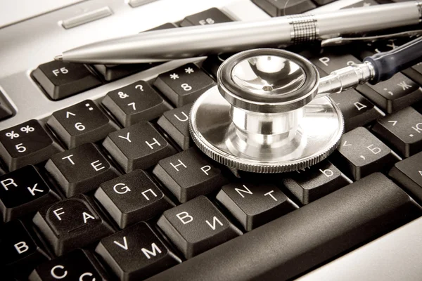 Shiny stethoscope and silver pen on keyboard — Stock Photo, Image