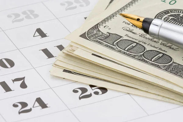 Inkoustové pero a dolar peníze na kalendáři — Stock fotografie