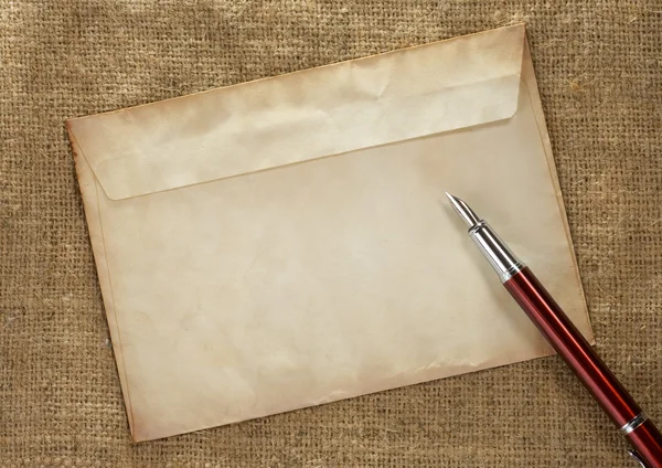 Чернильное перо в конверте на старинном фоне мешка — стоковое фото