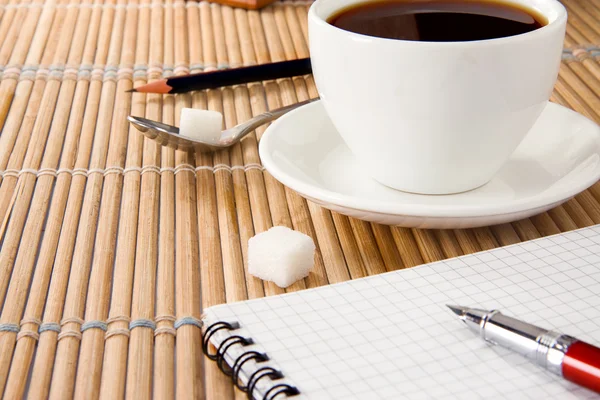 Šálek kávy, pera a tužky na notebook — Stock fotografie