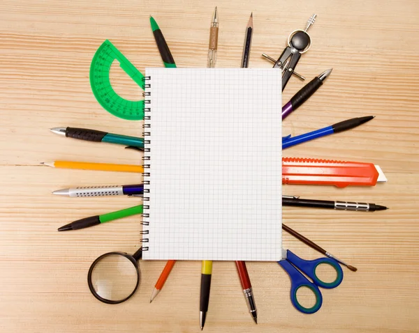 Bolígrafo, lápiz y lupa bajo cuaderno comprobado —  Fotos de Stock