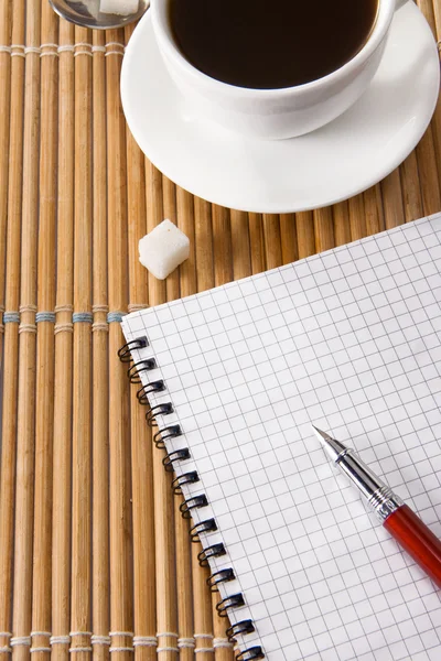 Šálek kávy a pera s notebookem na stole — Stock fotografie