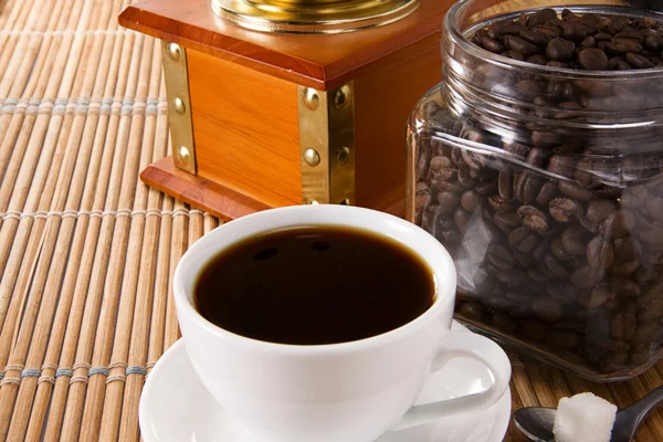 Cup of coffee, pot full of beans and grinder — Stock Photo, Image